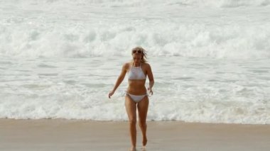 Seksi kadın okyanustaki kumlu bir sahilde koşuyor. Ağır çekimde.