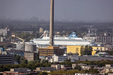 ROTTERDAM, NETHERLANDS - 13 Eylül 2025 - Rotterdam limanına yanaşmış sanayi bacası ve arka planında rüzgar türbinleri olan bir yolcu gemisi. ROTTERDAM, NETHERLANDS - 13 Eylül 2025 -
