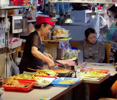 SEOUL, Güney Kore - 11 Ekim 2025 Seul 'deki geleneksel bir pazarda müşteriler için taze Kore sokak yemekleri hazırlayan kadın