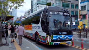 BUSAN, Güney Kore - 9 Ekim 2025 Busan Şehir Tur otobüsü kalabalık bir caddeye park edilmiş kaldırımda yürüyen insanlarla birlikte