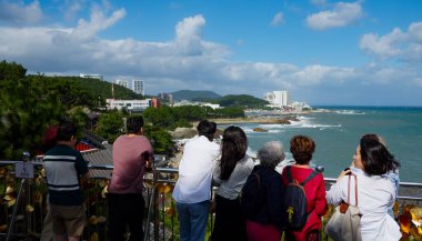 BUSAN, Güney Kore - 9 Ekim 2025 Haedong Yonggungsa Tapınağı yakınlarındaki bir gözlem güvertesinden kıyı manzarasının tadını çıkaran turistler