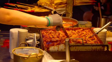 Şefin eli, gece pazarındaki sıcak tavadan bir porsiyon tteokbokki servis ediyor.