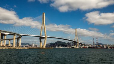 Busan Liman Köprüsü, şehir silüeti ve sanayi limanıyla denizi aşıyor.