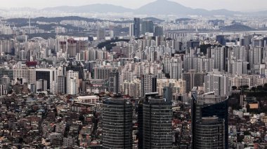 Seul metropolü yüksek binaları ve dağlara uzanan yoğun kentsel manzarayı gösteriyor.