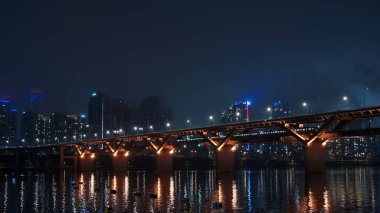Han Nehri Köprüsü ışıkları arka planda Seul şehir manzarasıyla birlikte karanlık suları yansıtıyor.