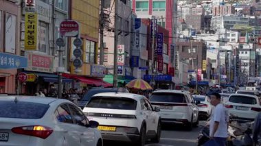 BUSAN, Güney Kore - 10 Ekim 2025 Kalabalık bir şehir caddesinde arabaların, binaların ve yayaların olduğu şehir sahnesi