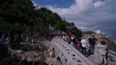 BUSAN, Güney Kore - 10 Ekim 2025 Haedong Yonggungsa Tapınağı 'ndaki geleneksel bir taş köprünün deniz manzarasının tadını çıkaran turistler