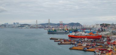 BUSAN, GÜNEY KOREA - 9 Ekim 2025 - Busan limanı büyük bir tersaneye demirli çeşitli gemiler ve bir şehir silueti