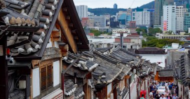 SEOUL, Güney Kore - 11 Ekim 2025 - Geleneksel Hanok çatıları, modern Seul siluetine bakan kalabalık bir cadde.