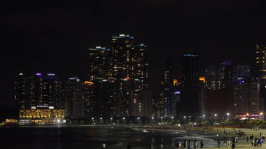 BUSAN, Güney Kore - 9 Ekim 2025 - Busan şehir silueti Haeundae Sahili 'ni aydınlatan insanlar gün batımından sonra suyun kenarında toplanıyor