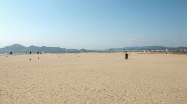 BUSAN, Güney Kore - 9 Ekim 2025 Dadaepo Sahili 'nde dağların altında kum ve denizin tadını çıkaran insanlar