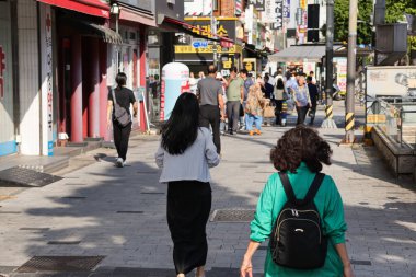 BUSAN, GÜNEY KOREA - 9 Ekim 2025 - Turistler ve yerliler kalabalık bir şehir caddesi boyunca dükkanlar ve işletmelerle birlikte yürüyorlar