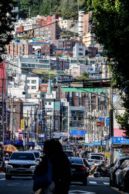 BUSAN, Güney Kore - 9 EKİM 2025 - Busan, Güney Kore 'deki bir yamaçta trafik ve binalarla dolu şehir caddesi