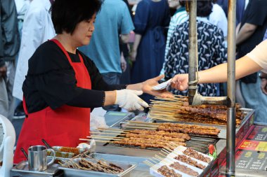 BUSAN, GÜNEY KOREA - 9 EKİM 2025 - Meşgul bir sokak yiyecek standında ızgara et şişleri hazırlayan ve satan tedarikçi
