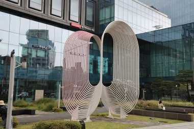 SEOUL, Güney Kore - 11 Ekim 2025 - Kamu parkındaki mimari ve yansımalarla çelişen soyut heykel