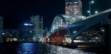 BUSAN, Güney Kore - 10 Ekim 2025 - Busan şehir manzarası modern bir köprü, aydınlık binalar ve gün batımından sonra kentsel su yolu