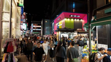 SEOUL, Güney Kore - 11 Ekim 2025 - İnsanlar geceleri Seul 'ün Myeongdong semtinde kalabalık bir sokakta alışveriş yapıp yürüyor