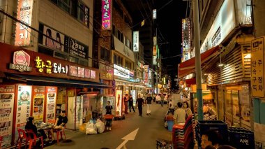 BUSAN, Güney Kore - 10 Ekim 2025 - Açık hava restoranlarında yemek yiyen ve neon tabelaların arasında yürüyen insanlarla sokak manzarası