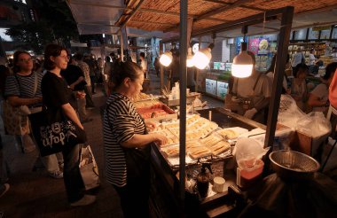 SEOUL, GÜNEY KORE - 11 Ekimde. 2025 - İnsanlar geceleri kalabalık bir marketten sokak yemekleri alıp yiyorlar.