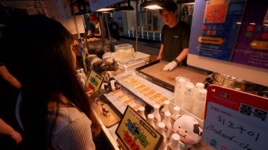SEOUL, GÜNEY KORE - 11 Ekimde. 2025 - Myeongdong, Seul 'deki bir sokak yemekçisinden popüler fırında peynir alan müşteri
