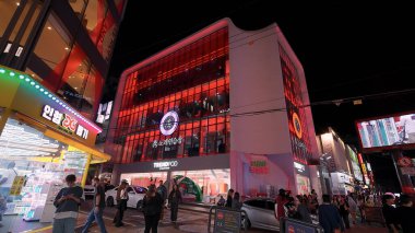 SEOUL, GÜNEY KORE - 11 Ekimde. 2025 - Seul Hongdae caddesi geceleri aydınlık binaların önünden renkli neon ışıklarıyla geçen insanlar