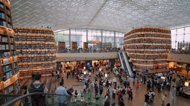SEOUL, GÜNEY KORE - 11 Ekimde. 2025 - Yükselen kitap rafları, yürüyen merdivenler ve atmosferden hoşlanan bir çok insan ile büyük bir kütüphane alanı