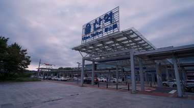 ULSAN, GÜNEY KORE - 10 EKİM. 2025 - Ulsan İstasyonunun dış cephesinde belirgin tabelaları, modern mimarisi ve arabalarla dolu işlek bir cadde yer alıyor