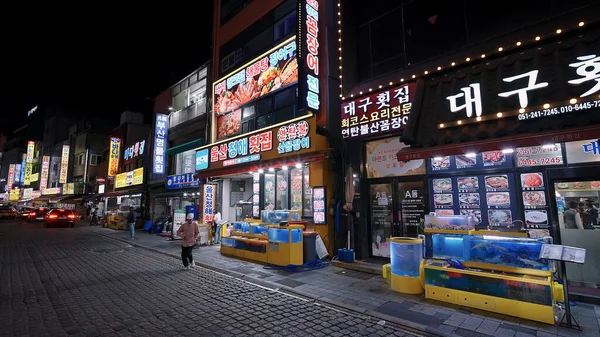 BUSAN, GÜNEY KORE 10 EKİM. 2025 - Busan, Güney Kore 'de aydınlatılmış deniz ürünleri restoranları ve açık hava tanklarıyla hareketli sokak sahnesi