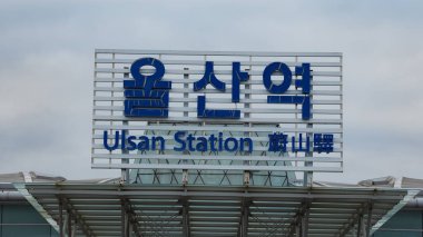 Bulutlu bir gökyüzüne karşı yolculara bilgi gösteren Ulsan İstasyonu işareti