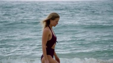 Şık bikinili bir kadın okyanusun kenarında zarif bir şekilde duruyor, sakin ve sakin sahil atmosferinin tadını çıkarıyor.