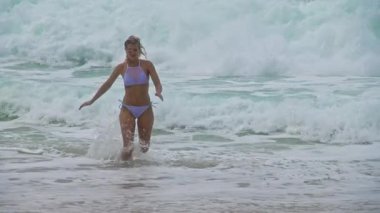 Neşeli bir kadın okyanus dalgalarını kucaklıyor, kumsaldaki parlak güneşin altında mutluluğu ve özgürlüğü somutlaştırıyor.