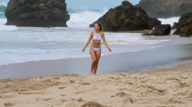 Neşeli ve kaygısız bir kadın büyük bir gülümsemeyle dalgalara doğru mutlu bir şekilde koşuyor.