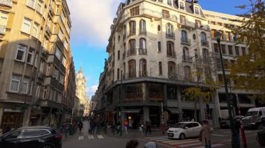 BRÜKSEL, BELGIUM - 26 Kasım 2025 - Tarihi mimarisi ve görünür bir kulesi olan şehir caddesinde yürüyen ve araba kullanan insanlar