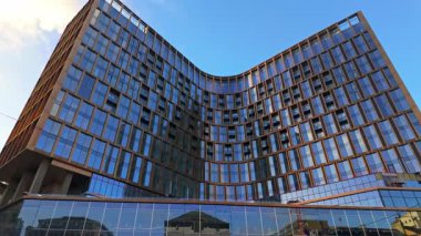 BRÜKSEL, BELGIUM - 26 Kasım 2025 - Mavi gökyüzü altında şehir renklerini yansıtan cam bir cephe içeren modern eğimli bina