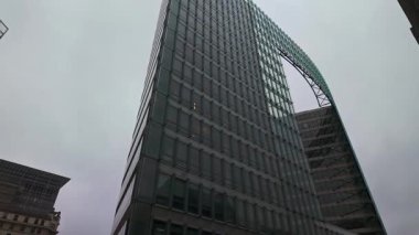 BRÜKSEL, BELGIUM - 26 Kasım 2025 - Çağdaş cam mimari ve bulutlu bir gökyüzüne karşı kemerli bir yapıya sahip gökdelen