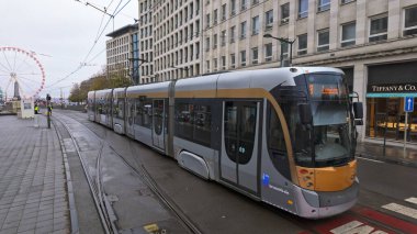 BRÜKSEL, BELGIUM - 26 Kasım 2025 - Arka planda dönme dolap ile şehir caddesinde hareket eden modern elektrikli tramvay