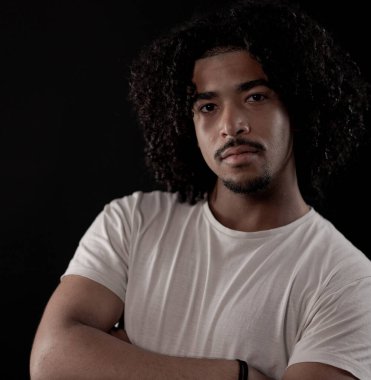 Siyah arka planda beyaz tişört giyen kıvırcık saçlı yakışıklı bir adamın stüdyo portresi. Bu moda ve güzellik portresi birçok ticari kullanım için mükemmeldir..