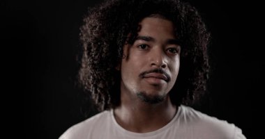 Siyah arka planda kıvırcık saçlı ve sakallı yakışıklı bir gencin stüdyo portresi. Bu görüntü moda ve güzellik projeleri için uygundur..