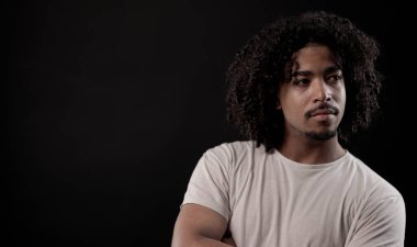 Siyah arka planda kıvırcık saçlı ve tişörtlü yakışıklı bir gencin stüdyo portresi. Bu görüntü moda ve güzellik kavramları için uygundur..