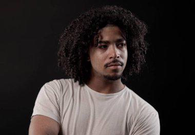 Siyah arka planda kıvırcık saçlı ve sakallı yakışıklı bir gencin stüdyo portresi. Bu görüntü modern ve kendinden emin bir erkek modelin sergilendiği moda ve güzellik projeleri için uygundur..