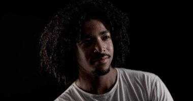 Siyah arka planda kıvırcık saçlı ve sakallı yakışıklı bir adamın stüdyo portresi. Bu görüntü moda ve güzellik projelerinin yanı sıra reklam kampanyaları için de uygun..