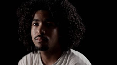 Siyah arka planda afro saçlı yakışıklı bir adamın stüdyo portresi. Bu görüntü moda ve güzellik projeleri için uygundur ve doğal ışık ile vesikalık çekimler için kullanılabilir..