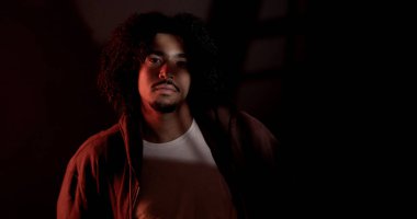 Stüdyo portresi, kıvırcık saçlı, kapüşonlu, siyah ışıklı bir genç adam. Bu görüntü moda güzelliği ve moda projeleri için uygundur..