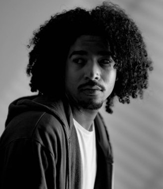 Siyah beyaz stüdyo portresi kıvırcık saçlı kapüşonlu genç bir adam. Bu moda ve güzellik konsepti imajı çeşitli ticari kullanımlar için uygundur..