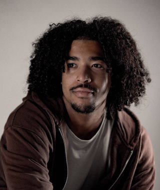 Kahverengi kapüşonlu bir kapüşonlu giyen, kıvırcık saçlı, yakışıklı Afro-Amerikan bir adamın stüdyo portresi. Bu moda ve güzellik konsepti, tarafsız bir arkaplanda çekilmiştir ve çeşitli ticari amaçlar için kullanılabilir..