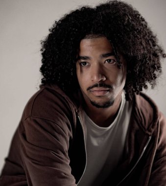 Kahverengi kapüşonlu, kıvırcık saçlı yakışıklı bir gencin stüdyo portresi. Bu görüntü moda güzelliği ve yaşam tarzı kavramları için kullanılabilir..