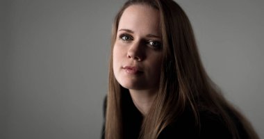 Uzun kahverengi saçlı ve gri arka planda yeşil gözlü güzel bir kadının stüdyo portresi. Bu görüntü moda ve güzellik projeleri, reklam kampanyaları ve başyazılar için uygundur..