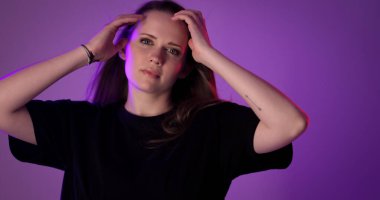 Güzel bir genç kadının stüdyo portresi. Elleri saçlarında, mor bir arka planda. Bu görüntü moda ve güzellikle ilgili projeler için uygundur..