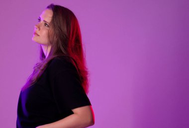 Mor bir arka planda poz veren uzun kahverengi saçlı güzel bir genç kadının stüdyo portresi. Bu görüntü moda güzelliği ve reklam projeleri için uygundur..