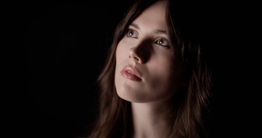 Kahverengi saçlı ve koyu arkaplana bakan güzel bir genç kadının stüdyo portresi. Bu görüntü moda güzelliği ve kozmetik kavramlar için uygundur..